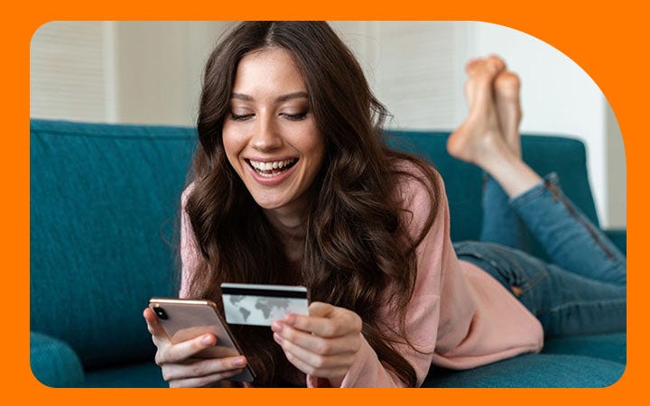 Mujer acostada en sillón con una tarjeta de crédito y un celular en mano