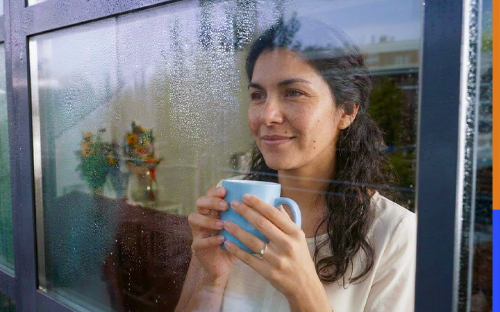 Persona con taza mirando por la ventana en día lluvioso