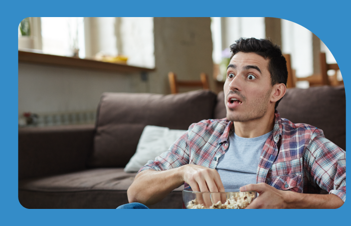 Hombre con cara de sorpresa sentado en un sillón comiendo cabritas
