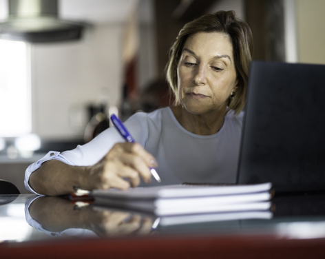 Mujer escribiendo en un cuaderno frente a un computador