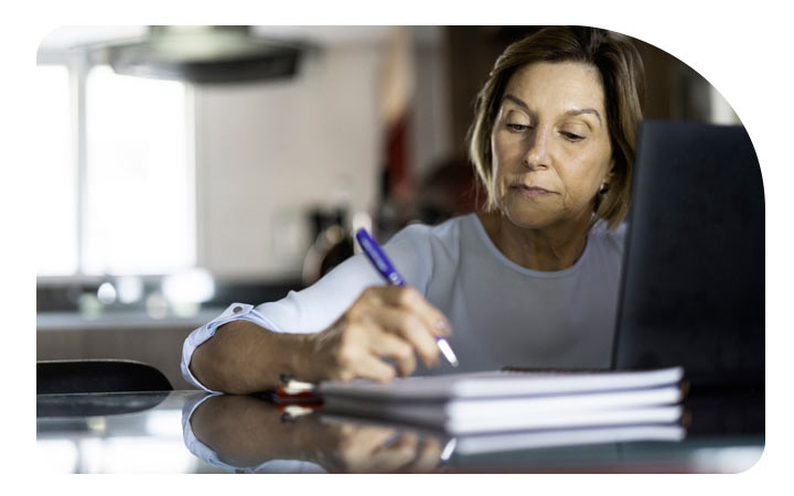 Mujer escribiendo en un cuaderno frente a un computador