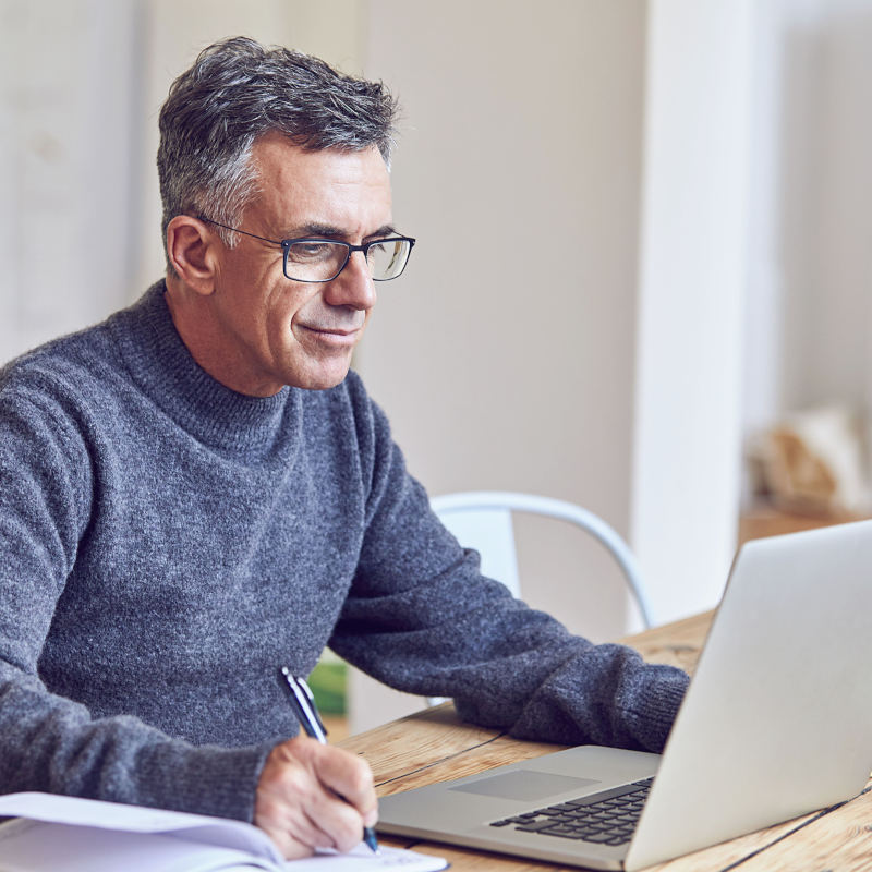 Hombre trabajando en su computador y escribiendo en una libreta Hombre trabajando en su computador y escribiendo en una libreta